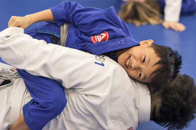 a boy smiling and practicing Jiu Jitsu with an adult at Gracie Barra Riverton