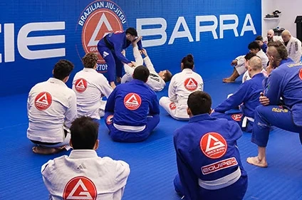 Students sitting on the mat watching a Brazilian Jiu-Jitsu technique demonstration at Gracie Barra Riverton